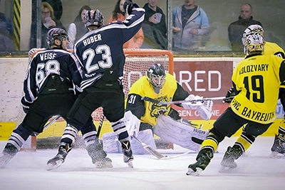 Ein intensiver Moment im Eishockey: Der Torwart in gelber Ausrüstung mit der Nummer 31 ist in Schussposition, umgeben von Spielern der Black Dragons Erfurt und eines gegnerischen Teams. Spieler "HUBER" (#23) und "WEISE" (#68) sind erkennbar. Eis spritzt im Bereich des Tores.